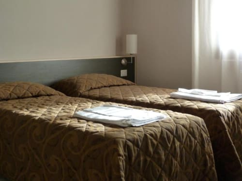 Camera dell'Hotel Eden a Vignola con letti gemelli, biancheria trapuntata marrone e luce naturale dalla finestra