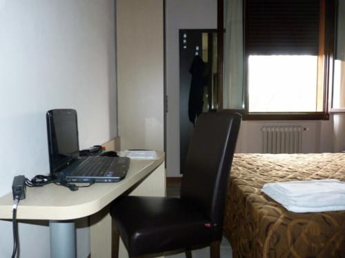 Camera d'albergo Eden a Vignola con scrivania, laptop, letto con biancheria a motivi e finestra con vista sui monumenti
