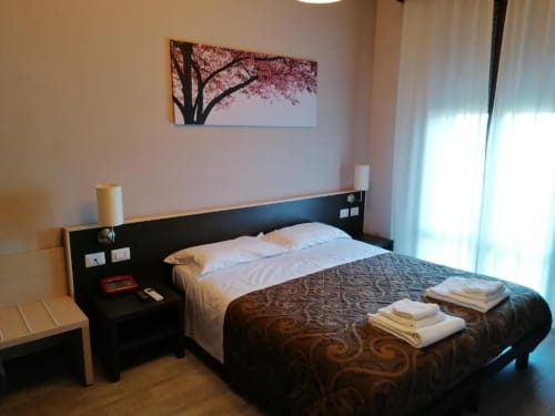 Camera moderna dell'Hotel Eden a Vignola con letto nero, biancheria bianca, dipinto floreale ciliegio rosa e luce naturale