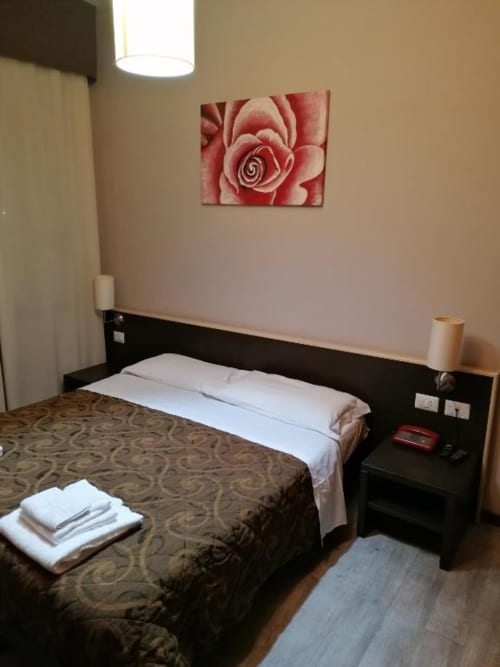 Camera Hotel Eden a Vignola con opere d'arte floreale, testata nera, cuscini bianchi e illuminazione calda