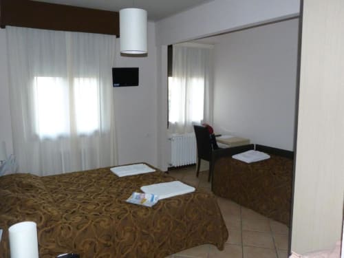Camera dell'Hotel Eden a Vignola con letto, specchio, scrivania e finestre con tende leggere
