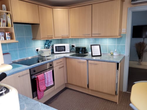 Modern kitchen in Jane's B&B apartment with light wood cabinets, blue tile backsplash, microwave, and appliances in