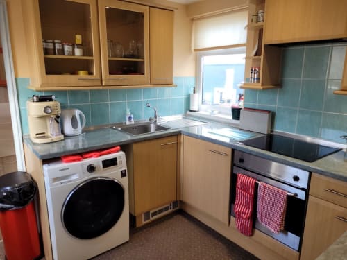 Modern kitchen with turquoise tiles, light wood cabinets, washing machine, oven, and sink at Jane's B&B apartment in