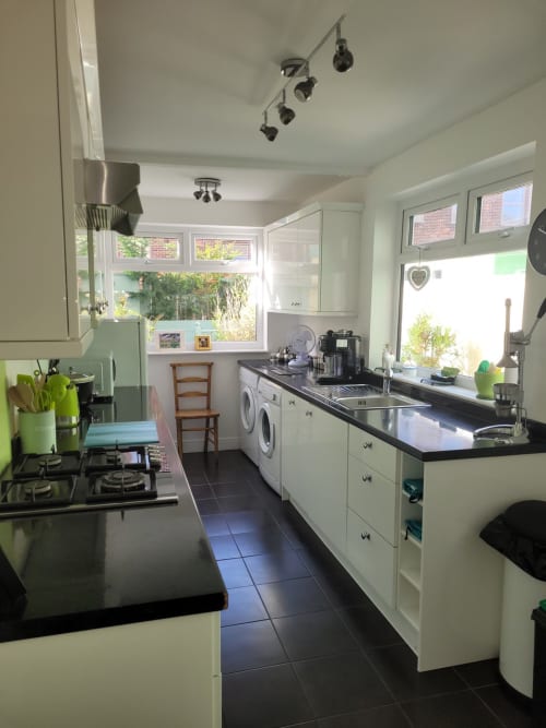 Modern kitchen with white cabinets, black countertops, washing machine, and large windows overlooking garden at Jane's B&B