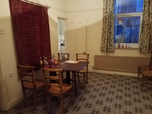 Dining area with wooden table and chairs, red wall tapestry, large window with patterned curtains at Jane's B&B villa