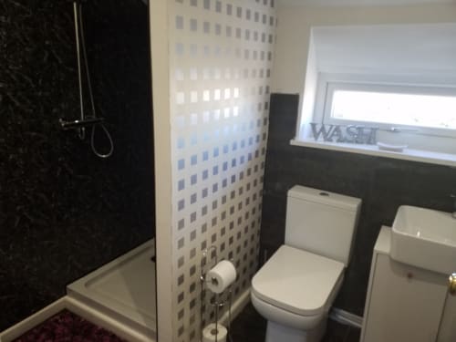 Modern bathroom at Jane's B&B villa in Guisborough with black shower cubicle, white toilet, sink, window with wash sign, and