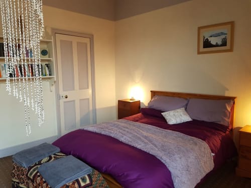 Cozy bedroom at Jane's B&B Lingdale villa with purple bedding, wooden bed frame, beaded chandelier, and warm lighting in