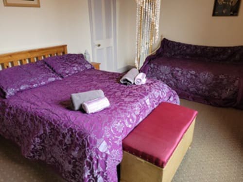 Purple quilted beds with white towels in Jane's B&B villa bedroom, Guisborough, with wooden frame and red ottoman visible