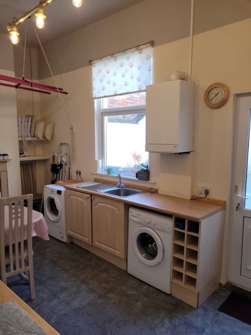 Modern kitchen with cream cabinets, washing machines, sink, and wooden countertop in Jane's B&B villa in Guisborough