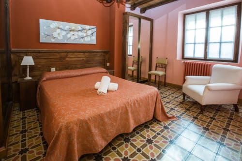 Dormitorio espacioso en Apartamentos Turísticos Ávila con paredes rojo-anaranjadas, cabecero de madera y suelo de azulejos tradicionales