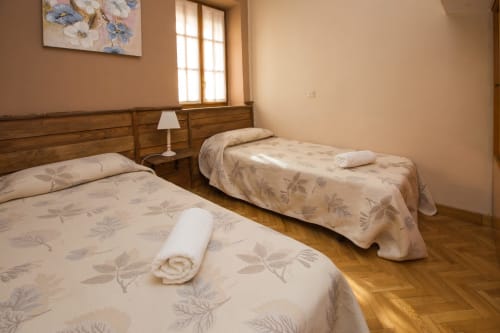 Habitación doble en Apartamentos Turísticos Ávila con camas de madera, toalla enrollada, lámpara de noche y ventana con vista a la ciudad