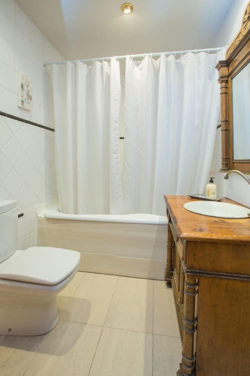 Baño moderno en apartamento de Ávila con azulejos blancos tipo metro, mueble de madera, inodoro y cortina de baño blanca