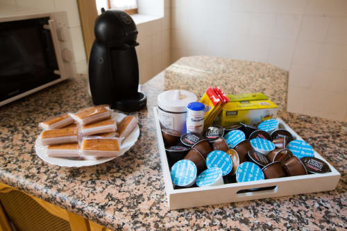 Amenidades de bienvenida en Apartamentos Turísticos Ávila con cafetera, chocolates, pastelería y artículos de tocador en la cocina