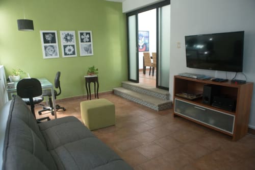Sala de estar moderna en Cozy House Downtown Cancún con paredes verde lima, sofá gris, TV, escritorio y acceso a terraza.