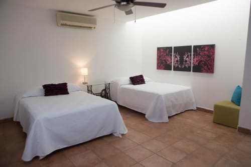 Habitación doble en Cozy House Downtown Cancun con camas blancas, arte púrpura, ventilador de techo y piso de terracota