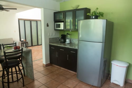 Cocina moderna de Cozy House Downtown Cancún con refrigerador de acero inoxidable, gabinetes negros, encimera de granito y detalles verdes