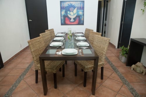 Comedor elegante con mesa larga, sillas tejidas y servicios de mesa en Cozy House Downtown Cancun