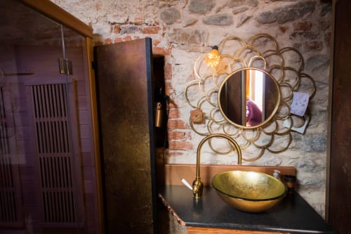Elegante mobile bagno nella spa CasaRosada di Vidracco con lavabo in ottone, specchio dorato e muri in pietra rustica.