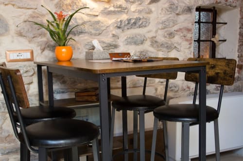 Zona pranzo moderna di CasaRosada con scrivania in legno, sedie nere, muro in pietra e pianta arancione a Vidracco, Italia