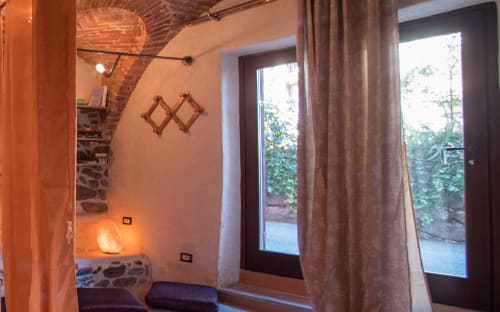 Romantica camera accogliente a CasaRosada con travi a vista, illuminazione calda, vista sul giardino attraverso porte vetrate e arredamento rustico