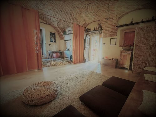 Spacious yoga and meditation studio at CasaRosada cottage in Vidracco with brick ceiling, cushions, and garden view