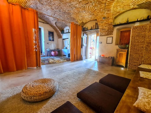 CasaRosada ALCHIMIA yoga studio with brick vaults, orange curtains, meditation cushions, and garden view in Vidracco