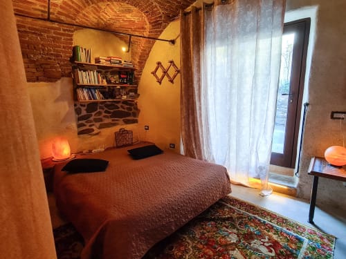 Camera accogliente a CasaRosada a Vidracco con illuminazione calda, mattoni a vista, letto, libreria e accesso alla terrazza