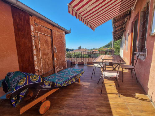 Sunny terrace at CasaRosada guesthouse in Vidracco with wooden deck, striped awning, dining table, and mountain views