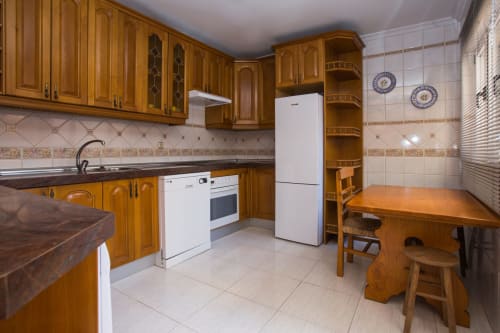 Amplia cocina con muebles de madera, electrodomésticos blancos, mesa y sillas de comedor en apartamento de Ávila
