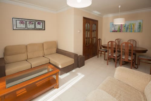Sala de estar y comedor moderno con sofá beige, mesa de madera y sillas de comedor en Ávila, España