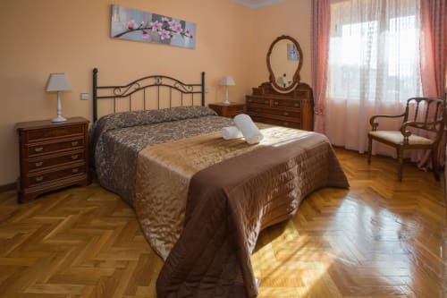 Espacioso dormitorio en Apartamentos Turísticos Ávila con cama doble, muebles de madera y vistas a la ciudad desde las ventanas