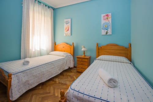 Dormitorio doble con paredes turquesas, camas de madera y cuadros florales en Apartamentos Turísticos Ávila, España