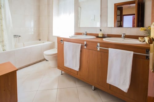 Baño moderno en Apartamentos Turísticos Ávila con vanidad de madera, doble lavamanos, bañera y pisos de cerámica