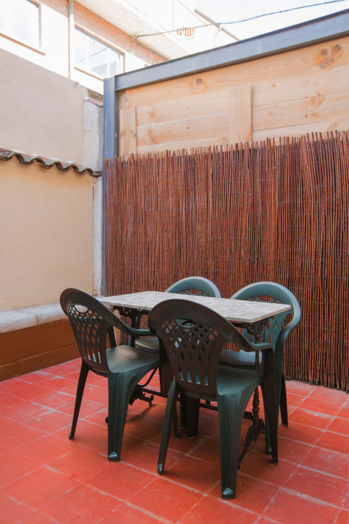 Patio exterior con mesa de comedor y sillas verdes en Apartamentos Turísticos Ávila, con piso de baldosas rojas y elementos de madera