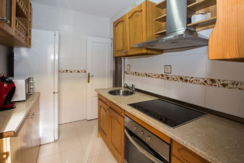 Cocina moderna en apartamento vacacional de Ávila con muebles de madera, campana extractora de acero inoxidable y comedor equipado