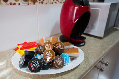 Cápsulas de café y snacks de waffle en plato blanco con cafetera roja en la cocina del apartamento de Ávila