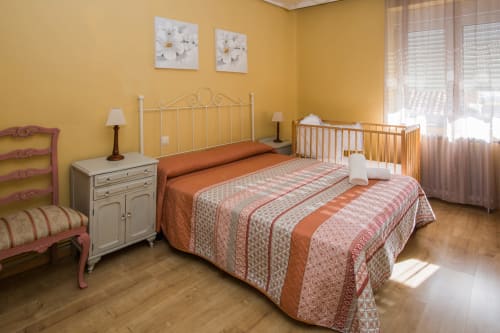 Dormitorio amarillo brillante con cama doble, cuna y silla rosa en apartamento Apartamentos Turísticos Ávila