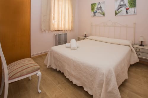 Habitación luminosa en Apartamentos Turísticos Ávila con cama matrimonial, cabecero blanco, suelo de madera y cuadro de la Torre Eiffel.