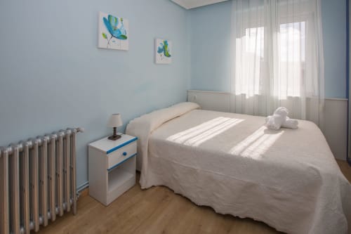 Dormitorio luminoso en Apartamentos Turísticos Ávila con cama blanca, mesita azul, radiador y arte mural colorido