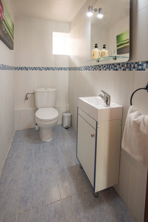 Cuarto de baño moderno en apartamento de Ávila con lavamanos blanco, inodoro, azulejo decorativo azul y espejo con iluminación