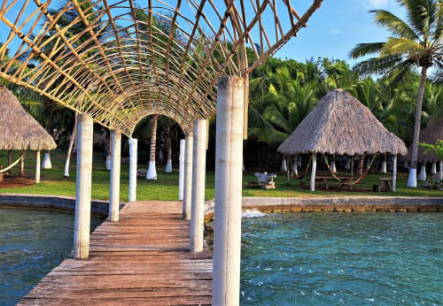 Muelle de madera con palapa de techo arqueado que se extiende hacia las aguas turquesas de la laguna en el albergue Cayuco Maya en Bacalar, México