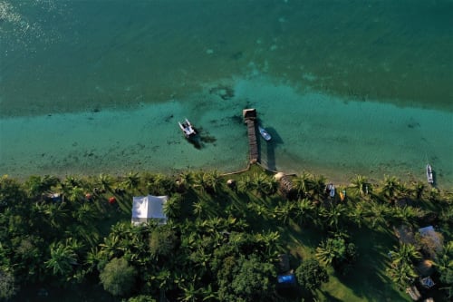 Vista aérea del muelle del hostal Cayuco Maya extendiéndose hacia la turquesa laguna de Bacalar con botes y palmeras