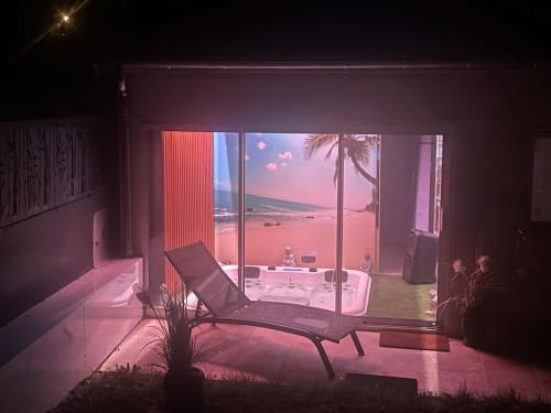 Le Gîte du Miroir lounge aux lumières roses ambiantes, méridienne et vue sur le coucher de soleil océanique par les portes vitrées