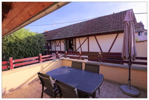 Terrasse du Gîte La Grange à Neuf-Brisach avec table à manger, parasol et maison à colombages