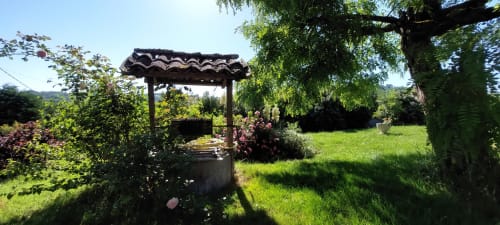 Wooden pergola over well in lush garden at Les Gites de Campardon, Monties France