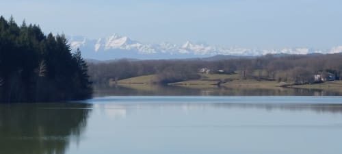 Serene lake view with snow-capped Alps, forests, and rural homes near Les Gites de Campardon, Monties France