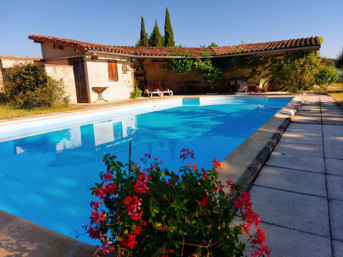 Les Gites de Campardon BnB pool in Monties, France with bright blue water, red flowers, and rustic terracotta-roofed building