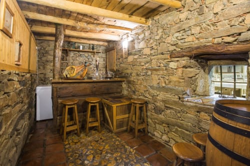 Rústica barra de piedra con taburetes de madera en casa rural de Ávila, con barril y vigas vistas