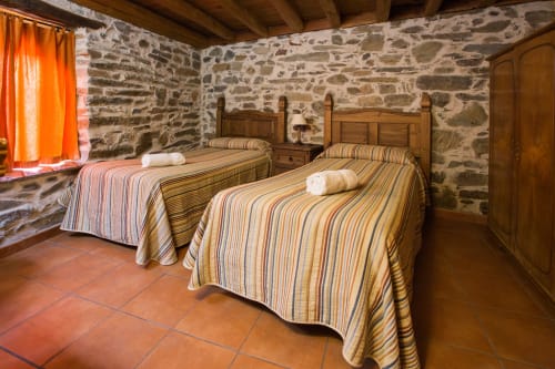 Dormitorio rústico en Apartamentos Turísticos Ávila con dos camas a rayas, muebles de madera y paredes de piedra