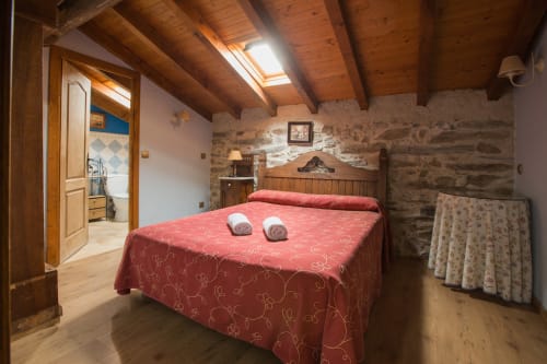 Dormitorio rústico en Apartamentos Turísticos Ávila con colcha roja, vigas de madera vista y paredes de piedra